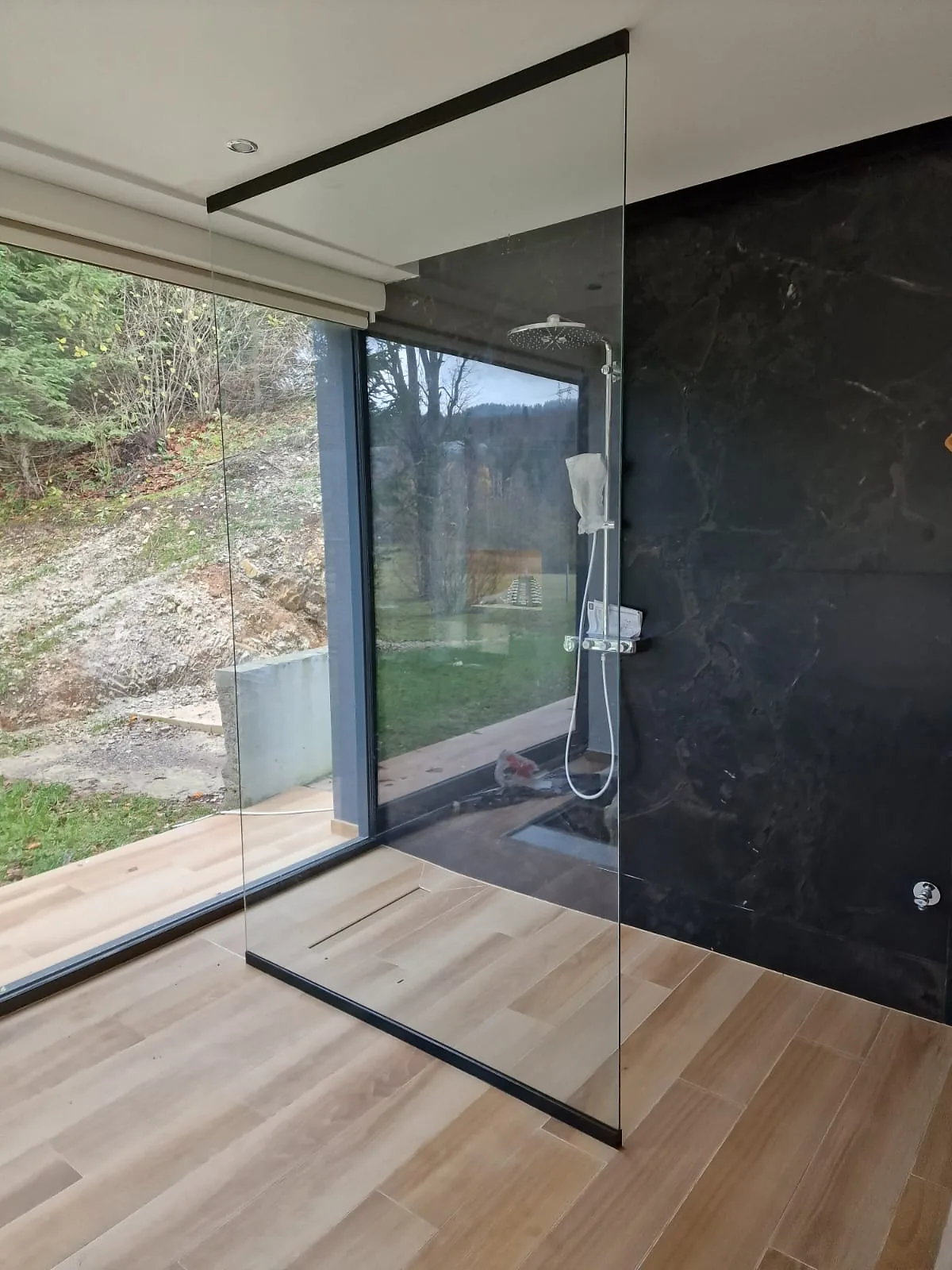 Walk-in tuš stijena s crnim nosačem uz panoramski prozor s pogledom na šumu
